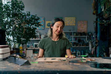 in a large green workshop, a woman with green hair creates decorative flowers laying them out on a...