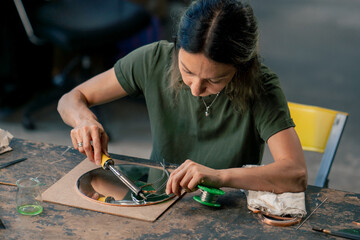 in a large green workshop, a woman with green hair creates decorative flowers laying them out on a...