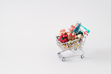 Shopping cart full of Christmas objects and decoration on white background with copy space.  Minimal Christmas and New Year concept. Creative festive holiday layout. Xmas aesthetic.