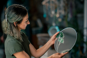 in a large green workshop, a woman with green hair has finished decorating a mirror with a glass...