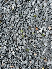 An array of small, gray stones fills the image, showcasing varied shapes and sizes, with a few green leaves interspersed among the gravel.