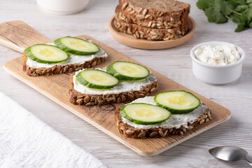 Slices of whole grain bread topped with cream cheese and fresh cucumber arranged beautifully at a rustic wooden table