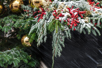 Christmas decoration made of fir branches, berries and toys on a table in the snow.