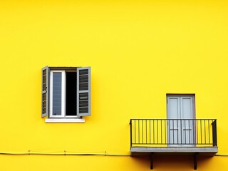 Obraz premium A lone window on a sunny yellow wall stands out with a balcony nestled beside it, sunlit yellow, yellow wall window balcony, garden views
