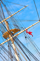 Fototapeta premium Blue sky, Denmark and travel with mast of ship outdoor in nature from below for culture or heritage. Adventure, engineering and rope with flag on sail boat for journey, holiday or vacation at sea