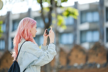 Fototapeta premium A woman with pink hair is taking a picture with her cell phone