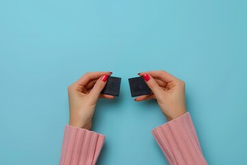 Fototapeta premium Hands Holding Two Small Black Squares on a Bright Blue Background