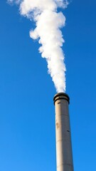Industrial pipe emitting white smoke contrasted against a clear blue sky, nature, pollutants, environment