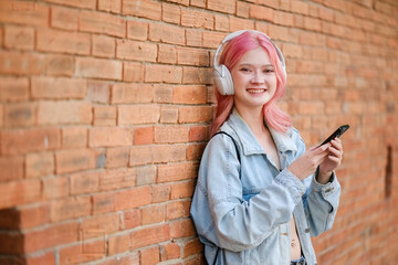 A girl with pink hair is holding a cell phone and wearing headphones