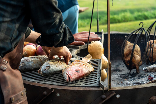 Whole fish being cooked on an open fire grill with squash and onions 