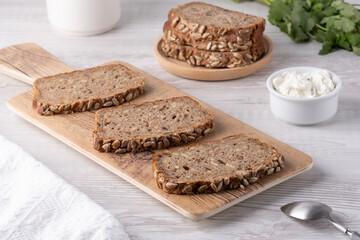 Freshly sliced whole grain bread served on a wooden board with cream cheese and herbs in a bright kitchen setting