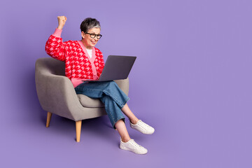 Full size photo of pretty retired female sit armchair hold netbook winning wear trendy red outfit isolated on purple color background