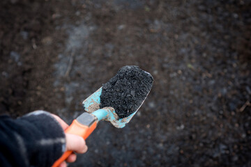 Close-up of biochar on a shovel, illustrating sustainable permaculture soil enhancement with Terra Preta
