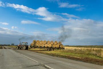 A tractor is pulling a trailer full of hay down a road © Sergei