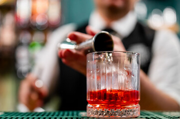 A bartender pours a drink into a textured glass, with a blurred background. The close-up shot captures the intricate details of the glass and the liquid, creating a dynamic and inviting scene