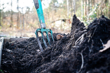 Close-up of a pitchfork in a raised garden bed filled with rich black compost and terra preta...