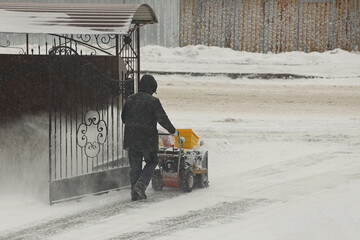 Worker clears snow from the sidewalk with a manual snowplow driven by a gasoline engine. Fighting...