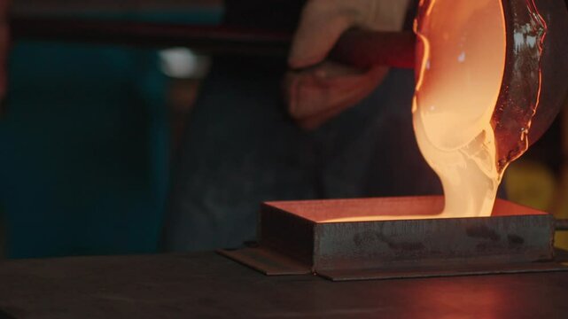 Two workers pour molten glass into a rectangular mold in a glassblowing studio