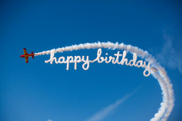 Fototapeta premium Plane writes Happy Birthday with smoke trail in blue sky, adding festive charm