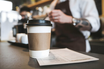 Disposable coffee cup with black lid on counter, cafe atmosphere in blurred background