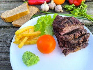 juicy steak on a white plate surrounded by vegetables.