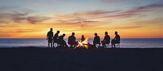 Foto op Canvas Silhouettes of friends gathered around a bonfire on the beach at sunset. © Muhammad