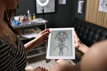Tattoo artist showing tablet with sketch to client in salon, closeup