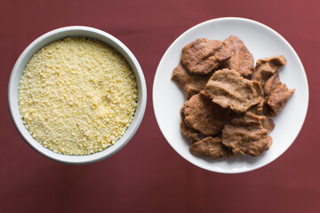 Overhead view of kuli-kuli and yellow garri in a white bowl, top view of nigerian groundnut cakes and garri in a bowl, fresh homemade nigerian kulikuli and cassava in a ceramic bowl
