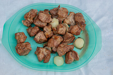 pieces of grilled pork meat with onions on a blue plate top view