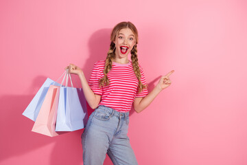 Joyful young woman with shopping bags pointing with excitement against pink background