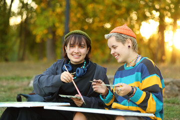 two young and innovative female artists conducting an outdoor painting lesson. Surrounded by...
