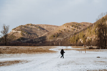 A person is leisurely walking through a beautiful snowy field while majestic mountains can be seen in the distant background, creating a picturesque winter landscape all around them