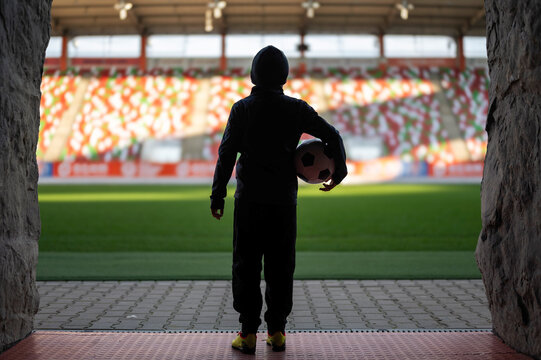 Young the boy with the ball standing in the players' tunnel and looking at the stadium