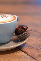 A creamy cappuccino with thick foam and a chocolate muffin, set on a saucer. This still-life composition captures the indulgence of a hot coffee drink paired with a light dessert.
