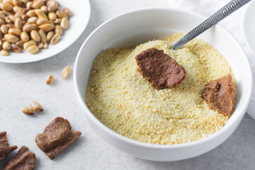 Overhead view of kuli-kuli and yellow garri in a white bowl, top view of nigerian groundnut cakes and garri in a bowl, fresh homemade nigerian kulikuli and cassava in a ceramic bowl