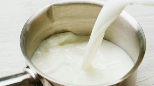 Milk pouring in pot stewpan glass cup close-up. Glass with yogurt, dairy products concept. Drinking fresh lactose-free milk in morning.