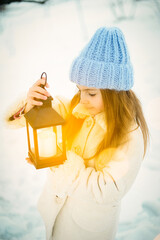 Girl in a blue hat holding a lantern against a snowy background. Magical winter atmosphere.