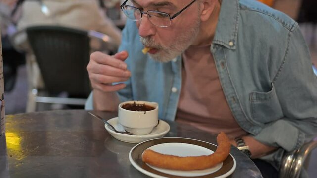 Elderly man with Parkinson's enjoying churros and chocolate, savoring a moment of indulgence