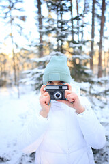 a woman holding a vintage camera, set against the stunning backdrop of a snowy winter forest. Dressed warmly for the cold, she embodies a sense of nostalgia and creativity, ready to capture the beauty