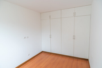 habitacion de departamento con closet empotrado o incorporado, con acabdos en melamina en habitacion moderna con piso de madera y paredes blancas