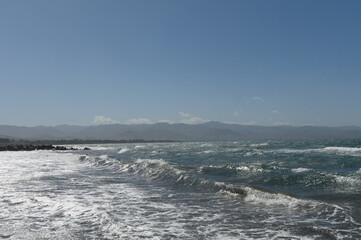 Waves gently roll onto a sandy beach under a clear blue sky on a sunny afternoon by the coastal shoreline