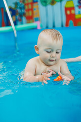 A 1-year-old boy learns to swim in a children's pool with a coach. Swimming courses for children. Children's pool.