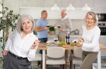 Happy party people celebrating friendship. Four mature friends dancing and singing at home. Cheerful women and men enjoy music together