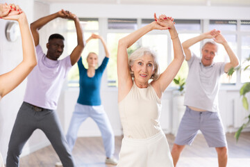 Naklejka premium Elderly woman and small group of amateur dancers of different ages are actively engaged in fitness room. Physical activity, good bodily shape