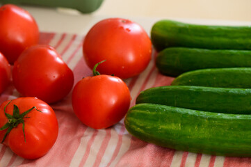 Fresh garden tomatoes and cucumbers arranged on a striped cloth for a summer meal preparation