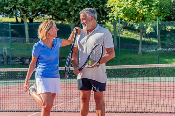 Senior couple smiling and stretching on tennis court before match
