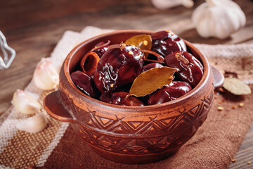 Bowl of pickled plums with spices on rustic wooden background. Clean eating, vegetarian food concept