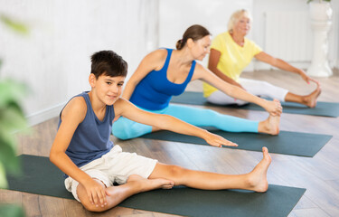 Obraz premium Positive preteen boy practicing head to knee pose of yoga on black rug with other persons