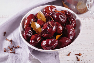 Bowl of pickled plums with spices on rustic wooden background. Clean eating, vegetarian food concept