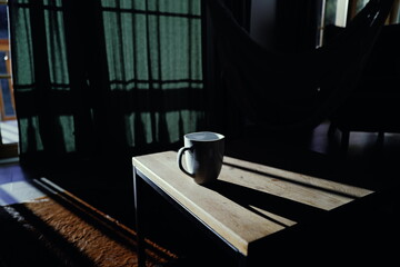 Stimmungsvolle Morgenlichtaufnahme einer Tasse Kaffee auf einem Holztisch in einem gemütlichen Raum